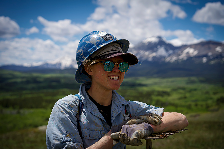 A volunteer smiling in a hard hat and work gloves on a sunny day